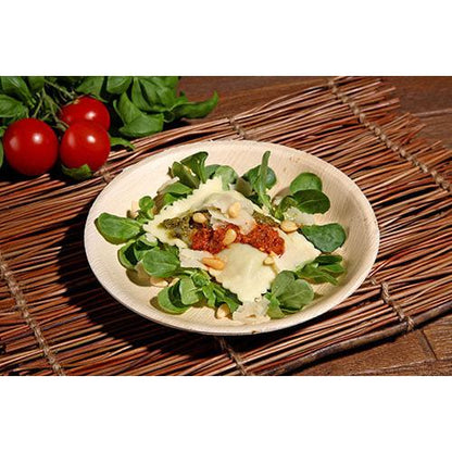 A plate of ravioli with pesto, sun-dried tomato sauce, pine nuts, and cheese is served on fresh greens in a PAPSTAR palm leaf bowl (17.5 cm), an environmentally friendly bowl from the 6-piece set by PAPSTAR GmbH, with tomatoes and leafy greens in the background.
