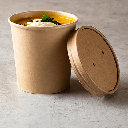 On a light stone surface stands a brown Starpak soup cup filled with soup, cream, and parsley. On top lies a Starpak 25 lid for soup cups, cardboard round.