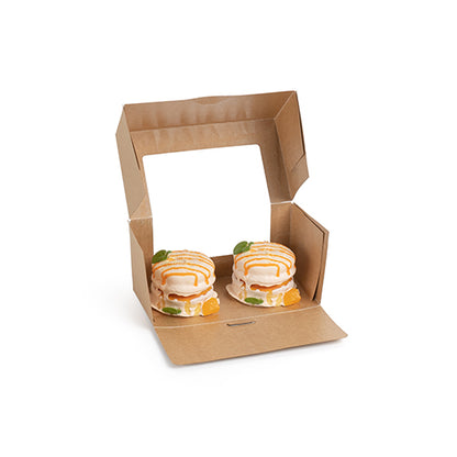 A PAPSTAR 25 cake boxes with a square lid with a PLA viewing window from PAPSTAR GmbH is open, showing two small round cakes with white icing, orange drizzle, and fruit pieces inside.