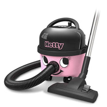 Der Hetty Compact Staubsauger HET160-11 der Numatic International GmbH ist ein rosa-schwarzer Kanistersauger mit einem lächelnden Gesicht, einem flexiblen Schlauch, einem fahrbaren Untersatz und einem Saugkopf, der neben dem Gerät auf dem Boden steht.