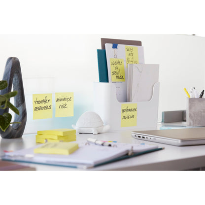 A modern office desk with a laptop, stationery, a white document tray, a small white turtle figurine, and 3M Deutschland GmbH Post-it® Super Sticky Notes Cube (Yellow, 76x76 mm) with the inscriptions "Transfer resources", "Minimize risk", and "Performance assessment".