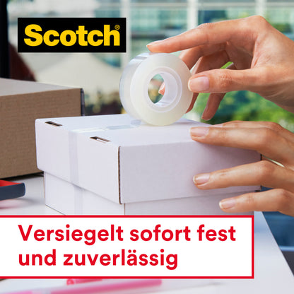 Eine Person verschließt eine weiße Schachtel mit Scotch® Crystal Klebeband, 19 mm x 25 m, 1 Rolle + 8 m GRATIS der 3M Deutschland GmbH. Auf dem Tisch stehen mehrere Schachteln und Büromaterialien. Deutscher Text: "Versiegelt sofort fest und zuverlässig.
