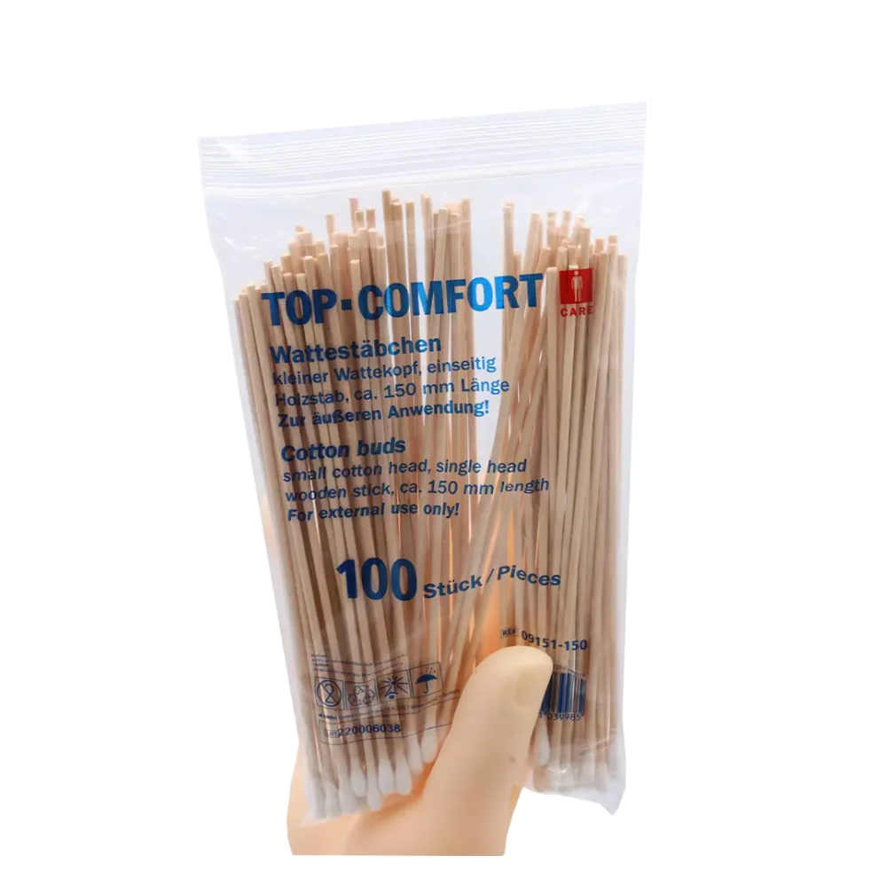 A hand holds a transparent plastic package with AMPri TOP-COMFORT cotton swabs, perfect for hospital care. The package contains 100 disposable cotton swabs with natural wooden sticks, product details are provided in both German and English.