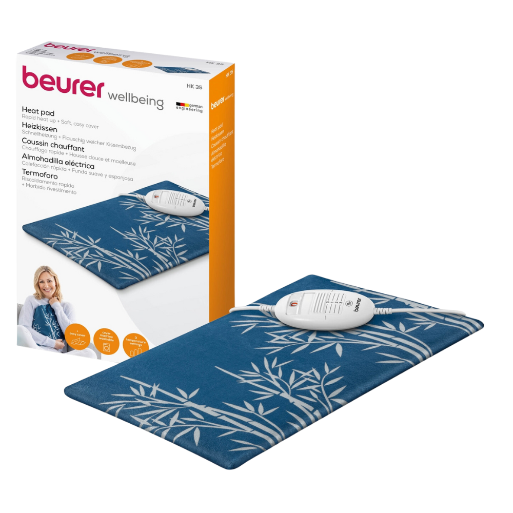 A Beurer HK 35 heating pad of the Beurer GmbH with a soft blue cover decorated with a white bamboo design is shown next to its packaging (1 piece). The heating pad features a control unit certified according to OEKO-TEX® STANDARD 100 and emphasizes comfort and quick heating for fast warmth.