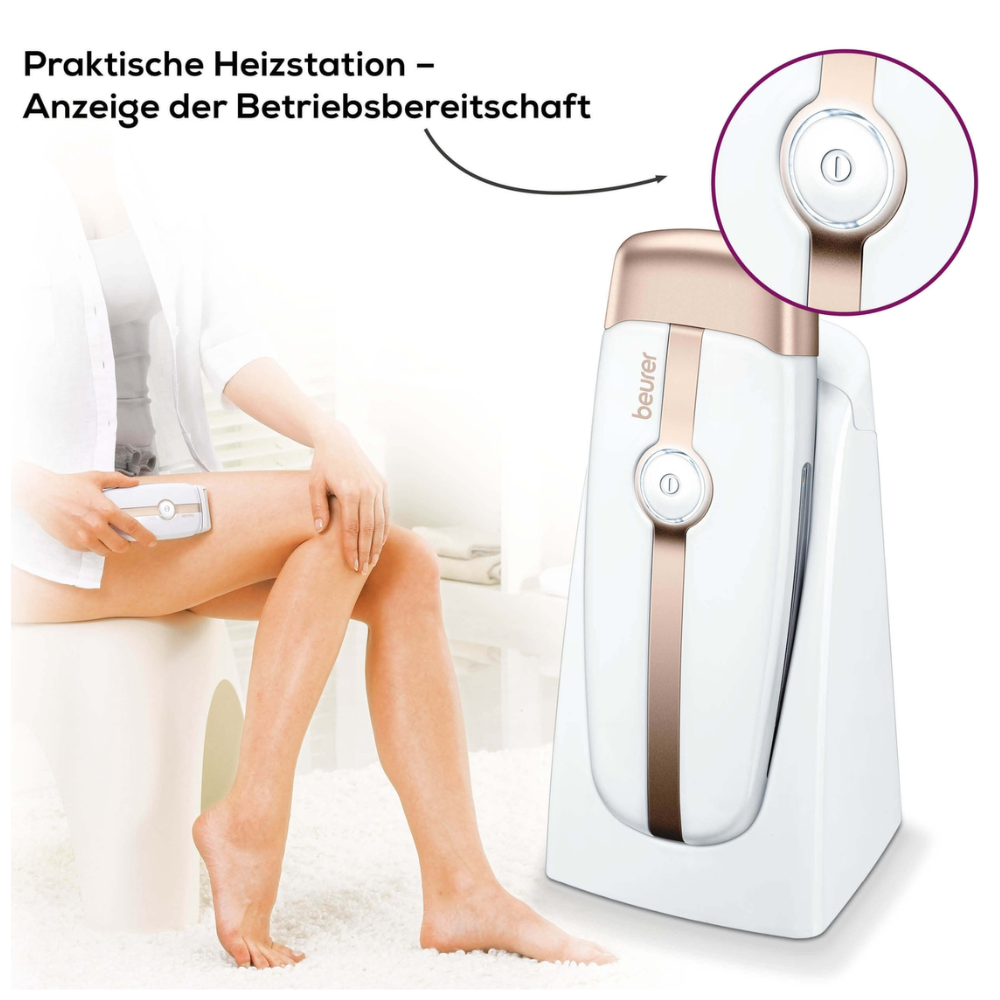 A person uses the Beurer HL 40 warm wax hair remover from Beurer GmbH on their leg. The text „Practical heating station – Operating status display“ indicates that the device has a practical heating station and an operating status indicator. The device is white and beige.