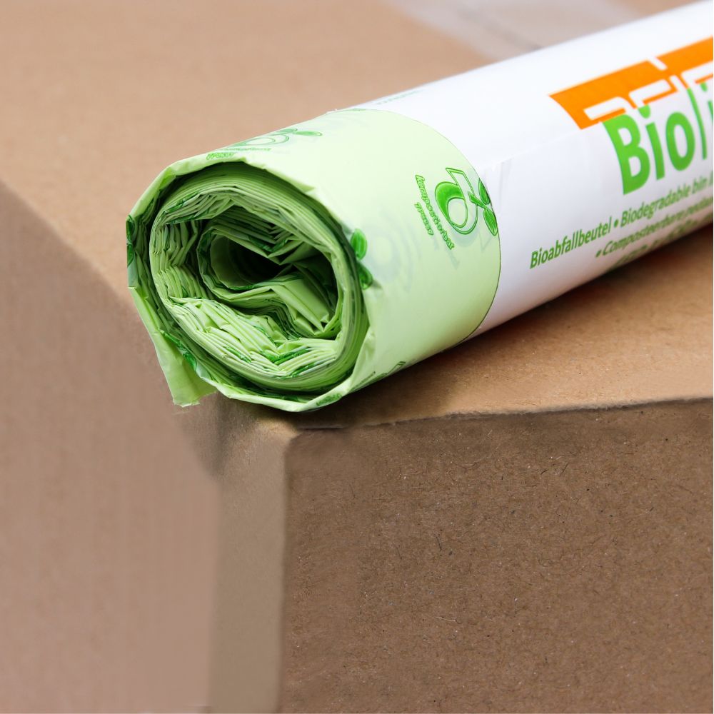 A roll of light green DEISS organic waste bags 30 liters, 06030, which are 100% compostable, lies on a brown box. The packaging is partially visible and shows an eco-friendly logo and the word "Bio" in bold orange letters of EMIL DEISS KG (GmbH + Co.).
