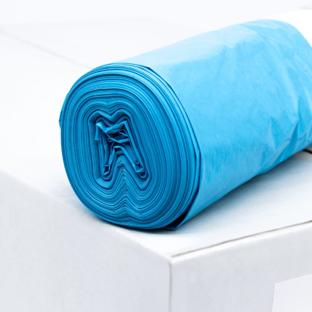 A roll of blue DEISS LDPE garbage bag Type 60, 20772, 70 liters from EMIL DEISS KG (GmbH + Co.) lies on a white box. These durable bags, known for their tear resistance, are neatly rolled to make the layered structure of the recycled material visible. The background remains simple and minimalist.