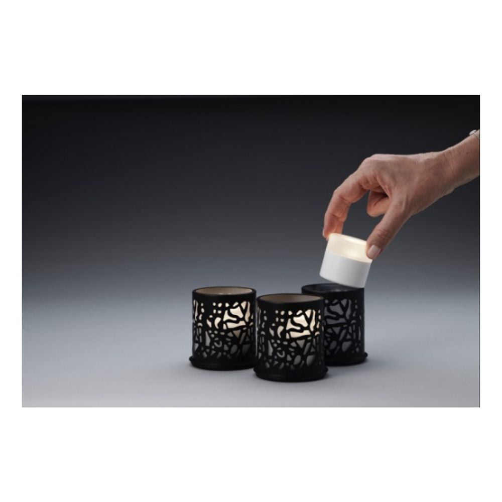 A hand lifts a small white LED candle from a black holder, while two identical Duni GmbH Multicolour LED Set, Mini - 8 pieces rest in similar holders on a gray surface against a dark background.