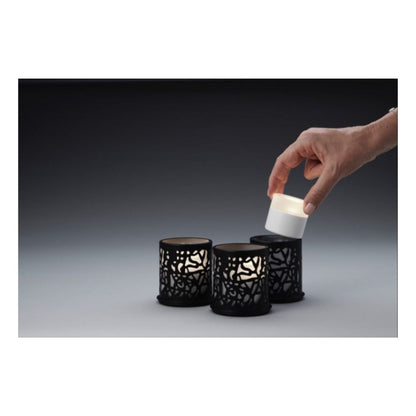 A hand lifts a small white LED candle from a black holder, while two identical Duni GmbH Multicolour LED Set, Mini - 8 pieces rest in similar holders on a gray surface against a dark background.