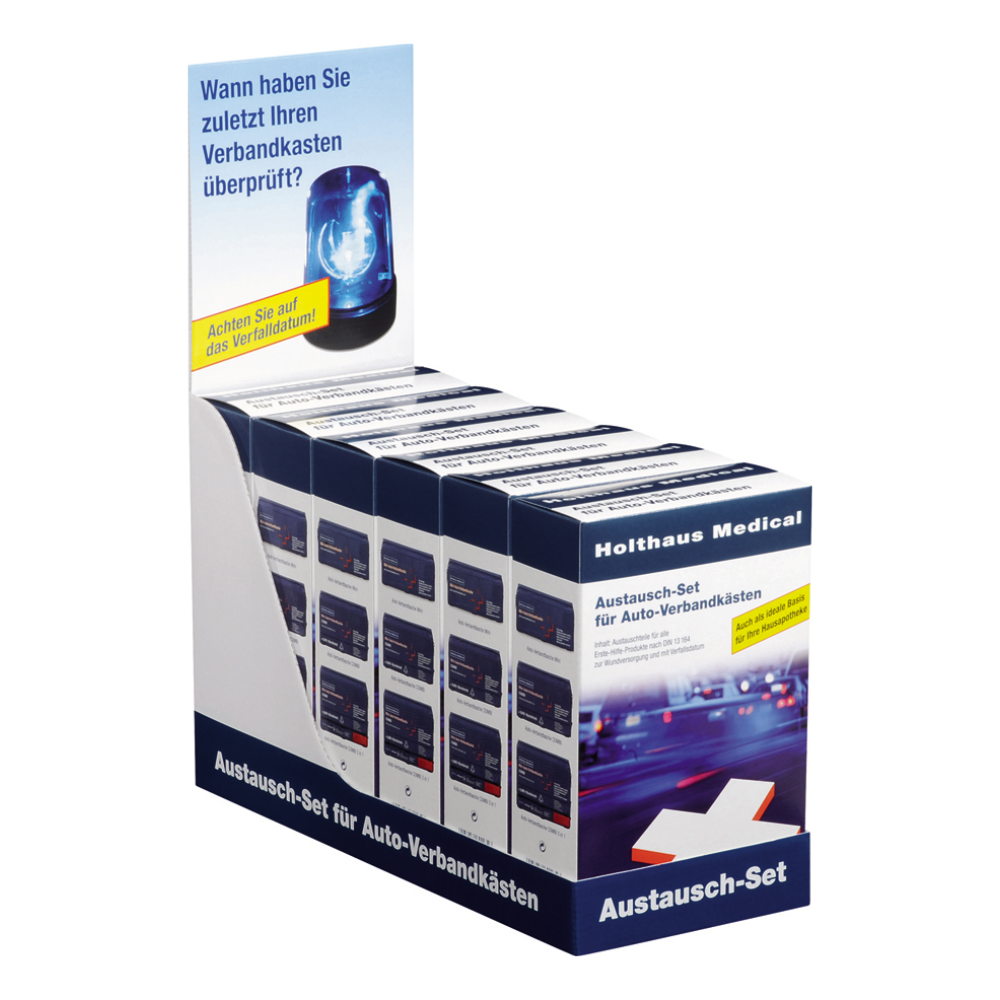 At an exhibition stand, there are several boxes labeled “Holthaus Replacement Set for Car First Aid Kits DIN 13157 | Package (1 piece)“ by Holthaus Medical GmbH & Co. KG. The stand features a header with the image of a blue emergency light and a German text urging the viewer to remember the last time they checked their first aid products or car first aid kits.