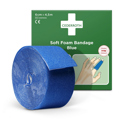 In front of a green packaging box, a roll of blue Holthaus plaster dispenser soft foam bandage with the inscription 6 cm x 4.5 m is presented. The box shows a hand with the bandage wrapped around a finger and bears the inscription "Cederroth Soft Foam Bandage Blue". This product fits perfectly with the refill roll soft foam from Holthaus Medical GmbH & Co. KG.
