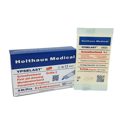 The image shows a Holthaus Ypselast® quick bandage from Holthaus Medical GmbH & Co. KG. On the left, there is a blue and white box with the inscription "Quick Bandage Size 2" measuring 6x8 cm. On the right, one of the elastic fixation bandages is shown in its white individual packaging.