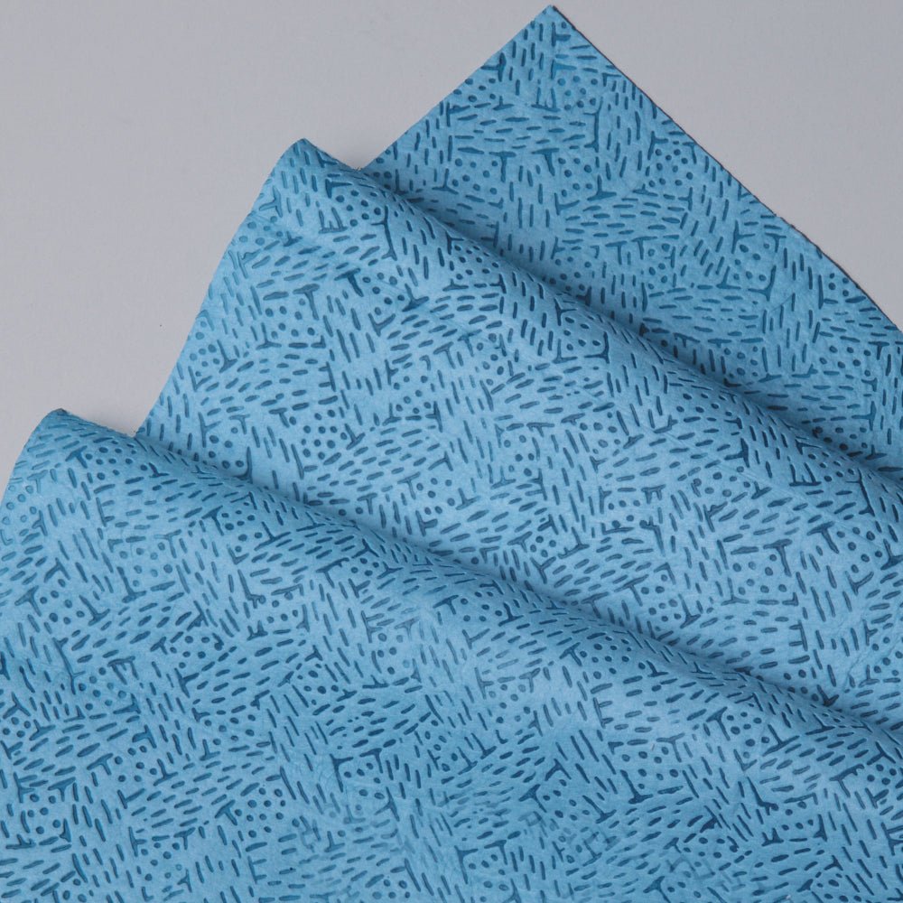 Close-up of folded Kimtech® process wipes (Kimberly-Clark GmbH) in blue, BRAG™ Box - 160 sheets, with geometric line and dot pattern. Ideal for demanding industrial cleaning. Displayed on a light gray surface.