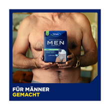 Ein Mann ohne Hemd hält eine Schachtel Muster TENA Men Active Fit Pants Normal Grey von TENA - Essity Germany GmbH in Brusthöhe. Der Text "Für Männer gemacht" betont den diskreten Schutz und Komfort für Männer mit Inkontinenz - für Männer gemacht.