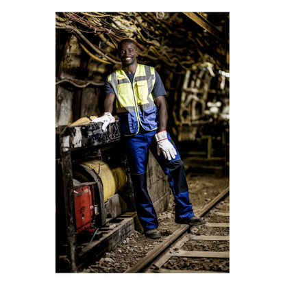 A worker wearing a NITRAS MOTION TEX LIGHT T-shirt with UV protection, certified by OEKO-TEX and manufactured by AS Arbeitsschutz GmbH, stands next to industrial equipment in an underground tunnel, surrounded by cables and machines.