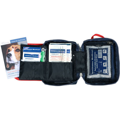 The Holthaus Medical Pet Care first aid bag from Holthaus Medical GmbH & Co. KG is a red first aid kit with bandages, antiseptic wipes, and other medical supplies in separate compartments. On the left side, there is a booklet with a dog face for the emergency care of your pet.