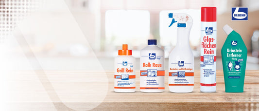 Eine Reihe von fünf Reinigungsprodukten der Marke Dr. Beckmann, angeordnet auf einer Holzoberfläche vor einem unscharfen Hintergrund. Zu den Produkten gehören Grill Rein, Kalk Raus, Feuchte Reinigungstücher, Glasflächen Rein und Urinstein Entferner.