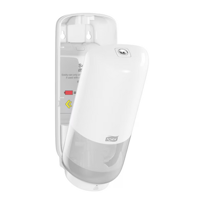 The wall-mounted Tork 561600 Skincare Dispenser with Intuition Sensor Elevation S4 by TORK - Essity Professional Hygiene Germany GmbH features an open front cover in white. The transparent lower part allows a view of the soap container, while installation and refill instructions as well as arrows are displayed in the open interior, ensuring easy maintenance of the touchless dispensing function.