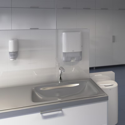 A modern public bathroom is equipped with a stainless steel sink and faucet, with a Tork 561600 Skincare Dispenser with Intuition Sensor Elevation S4 for soap on the left. The paper towel dispenser on the right ensures hygiene with intuitive touchless dispensing. The setup is completed with white-tiled walls and cabinets.
