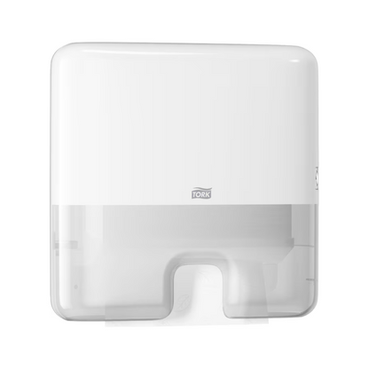 The Tork Xpress® 552100 Mini Dispenser for Multifold Hand Towels Elevation H2, offered by TORK – Essity Professional Hygiene Germany GmbH, is a wall-mounted white paper towel dispenser with a rectangular shape and a small bottom opening for single sheet dispensing. The brand logo is prominently displayed on the front, while the translucent section allows a view of the multifold towels inside.