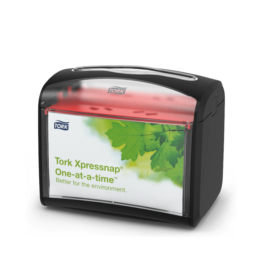 The Tork Xpressnap® 272611 table napkin dispenser by TORK – Essity Professional Hygiene Germany GmbH features a black top and a transparent front with a green leaf design and the inscription "Tork Xpressnap One-at-a-time – better for the environment." This dispenser improves hygiene while efficiently reducing napkin consumption.