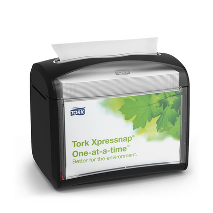 A black Tork Xpressnap® 272611 table napkin dispenser, distributed by TORK – Essity Professional Hygiene Germany GmbH, is presented with a label featuring green leaves and the message "Individually. Better for the environment." A single napkin is partially dispensed from the top to promote hygiene and efficient napkin use.