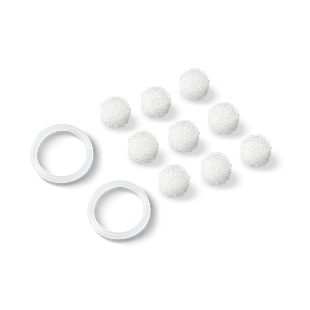 On a white background, eight small, round white objects resembling cotton balls are visible and arranged in a triangular formation. Two white plastic rings, probably replacement filters for the product "Beurer FC 40 Replacement Filters for Pore Cleanser | Pack (20 pieces)" by Beurer GmbH, are placed to the left of the cotton balls.