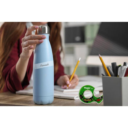 A person holds a light blue water bottle with the inscription "Hannah" at a desk with notebooks, pencils, a pen holder, and a pack of 3M Deutschland GmbH Scotch® Magic™ Invisible Tape 8-1925R3 (19 mm x 25 m, 3 rolls/pack).