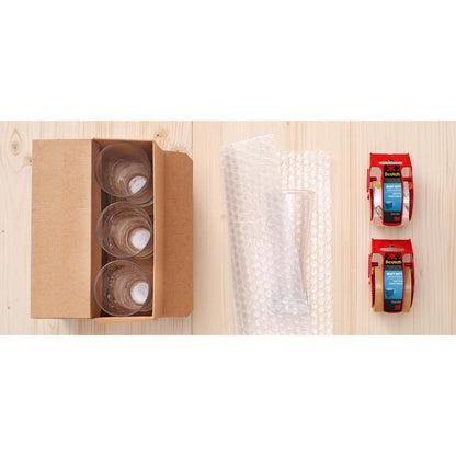 A box with four glass cups, bubble wrap, and 3M Scotch® Extra strong packaging tape (brown, 48 mm x 20.3 m, 1 roll on hand dispenser/package) on a light wood surface.