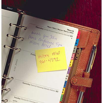 An open leather-bound planner shows handwritten Thursday notes: "Lunch 1 PM John," "Press conference 5 PM Hilton Hotel." On a yellow Post-it® Recycling Notes block from 3M Deutschland GmbH it says: "Hilton Hotel 761-4392." The dividers are visible.