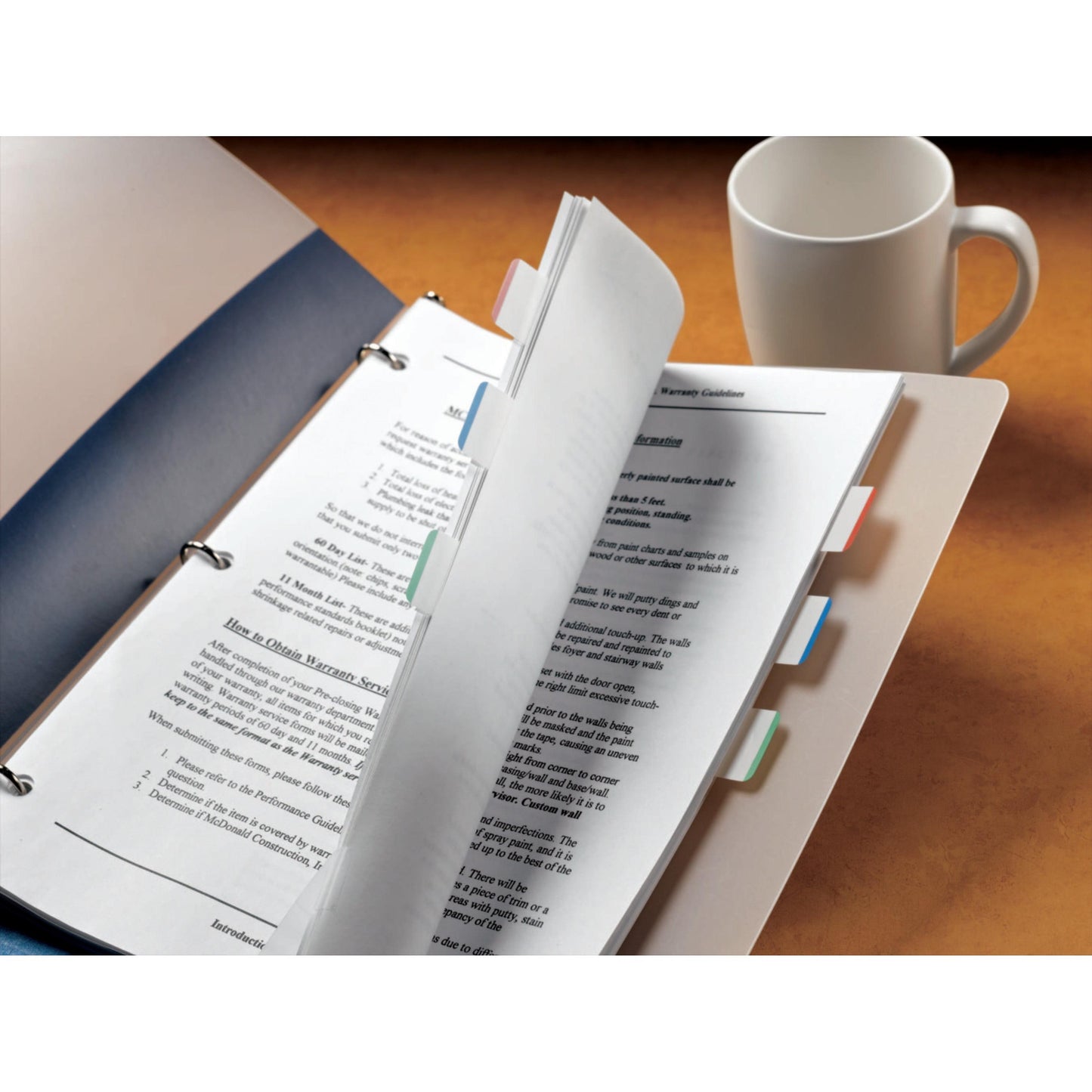 A folder with 3M Deutschland GmbH Post-it® Index Strong Filing Tabs (standard, various colors, 25.4 mm x 38.1 mm) and printed documents lies open on a desk next to a white mug, reflecting organization and paperwork.