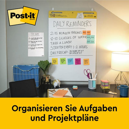 A desk with office supplies, lamp, and chair stands in front of a wall-mounted 3M Post-it® Super Sticky self-adhesive Meeting Chart (63.5x76.2 cm, 30 sheets) that shows daily reminders and notes. On a yellow banner below it says "Organize tasks and project plans."