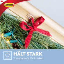 Ein Command™ Mini-Haken, transparent (3M Deutschland GmbH), wird rückstandsfrei auf Holz angebracht und hält einen Kieferzweig-Bündel mit roter Schleife (bis 225g). Text: "HÄLT STARK Transparente Mini-Haken".