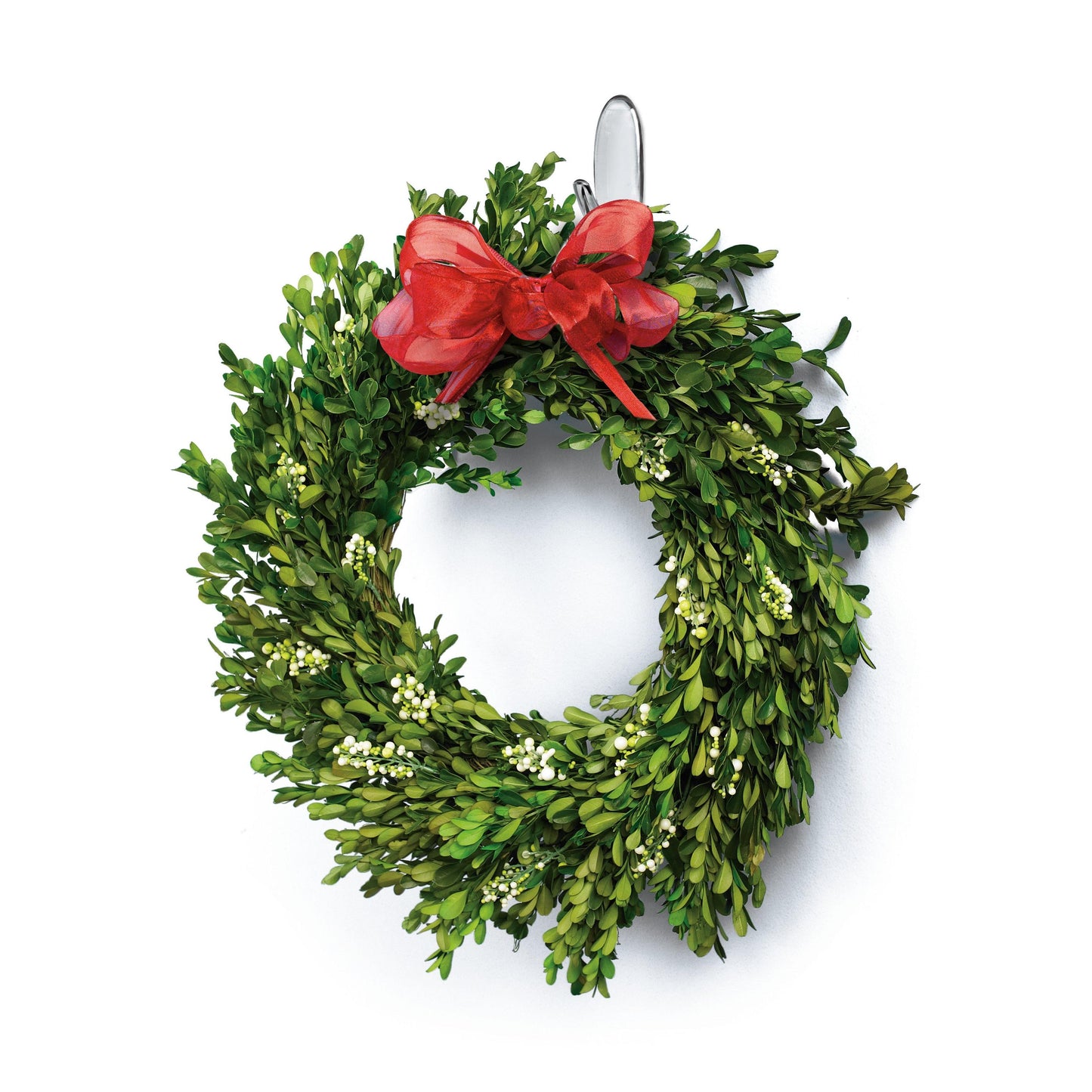 Ein grüner Buchsbaumkranz mit weißen Beeren und einer großen roten Schleife hängt an einem 3M Command™ Haken M, mittelgroß, transparent mit transparenten Strips, 17091CLR von 3M Deutschland GmbH vor einem weißen Hintergrund.