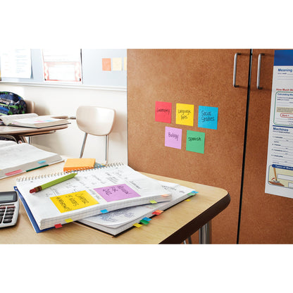 Auf dem Schreibtisch eines Klassenzimmers liegen aufgeschlagene Hefte, Papiere, ein Taschenrechner und Post-it® Super Sticky Notes (76 x 127 mm, 90 Blatt/Block, 100% PEFC) von 3M Deutschland GmbH. An einem Schrank in der Nähe sind bunte Zettel mit Fachbezeichnungen angebracht.