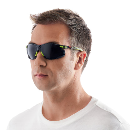 Ein Mann mit kurzen braunen Haaren trägt ein weißes T-Shirt mit Rundhalsausschnitt und eine 3M™ Solus™ Schutzbrille 1000 Sonnenbrille (Grün/Schwarz, graues Glas, Scotchgard™ Antibeschlag-Beschichtung) von 3M Deutschland GmbH vor einem schlichten weißen Hintergrund.