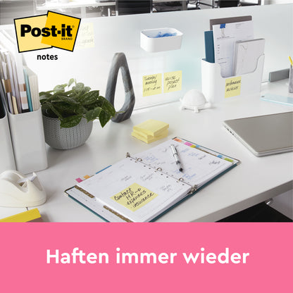 Ein moderner weißer Schreibtisch mit Schreibwaren, einer Pflanze, einem Laptop und Post-it® Notes (Gelb, 76x76mm, 100 Blatt/Block) von 3M Deutschland GmbH auf dem Schreibtisch und der Trennwand. Der deutsche Text lautet "Haften immer wieder". Ein offener Planer zeigt handschriftliche Notizen.