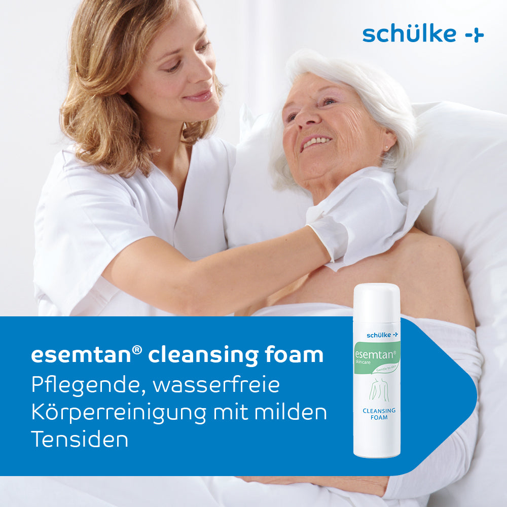 A caregiver in a white coat gently washes the shoulder of an elderly woman in bed. In the foreground, a 500 ml bottle of Esemtan® cleansing foam from Schülke & Mayr GmbH can be seen, which describes the gentle cleansing of the skin.